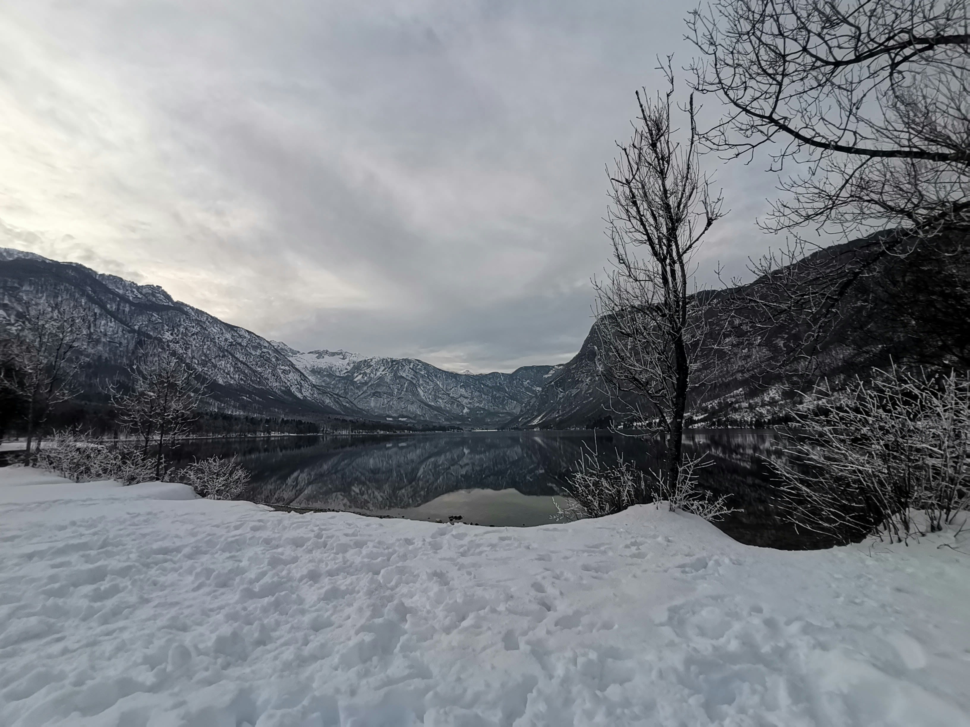 a lake surrounded by snow covered mountains under a cloudy sky